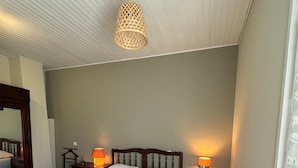 Une chambre à coucher avec un lit en bois, deux tables de chevet avec des lampes, une chaise en bois, une table en bois et un luminaire suspendu.