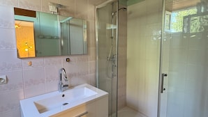 Une salle de bain avec une douche à parois de verre, un lavabo blanc avec un miroir au-dessus, et un plafond en bois.