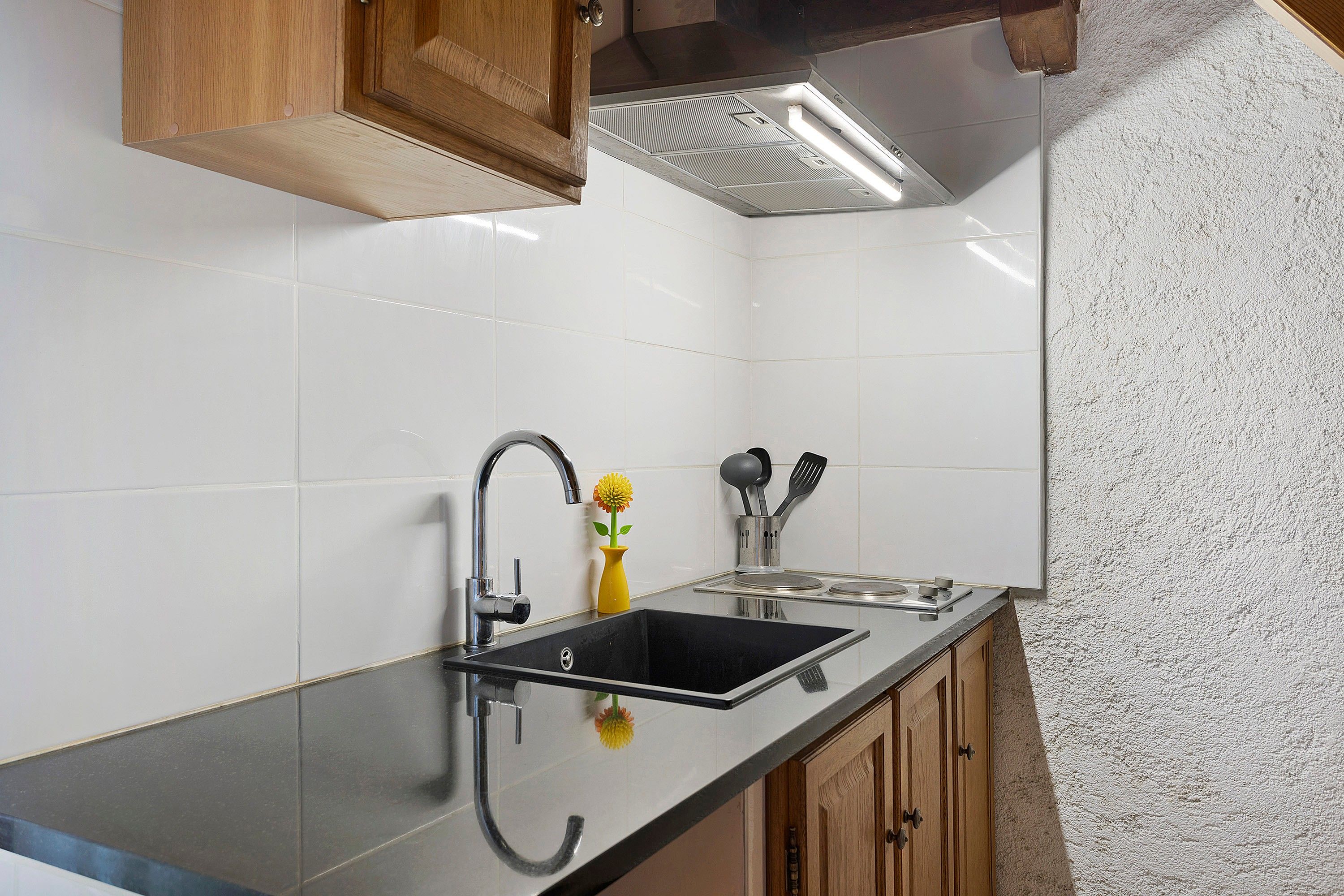 Een keuken met een zwart aanrecht, een roestvrijstalen spoelbak en houten kastjes.