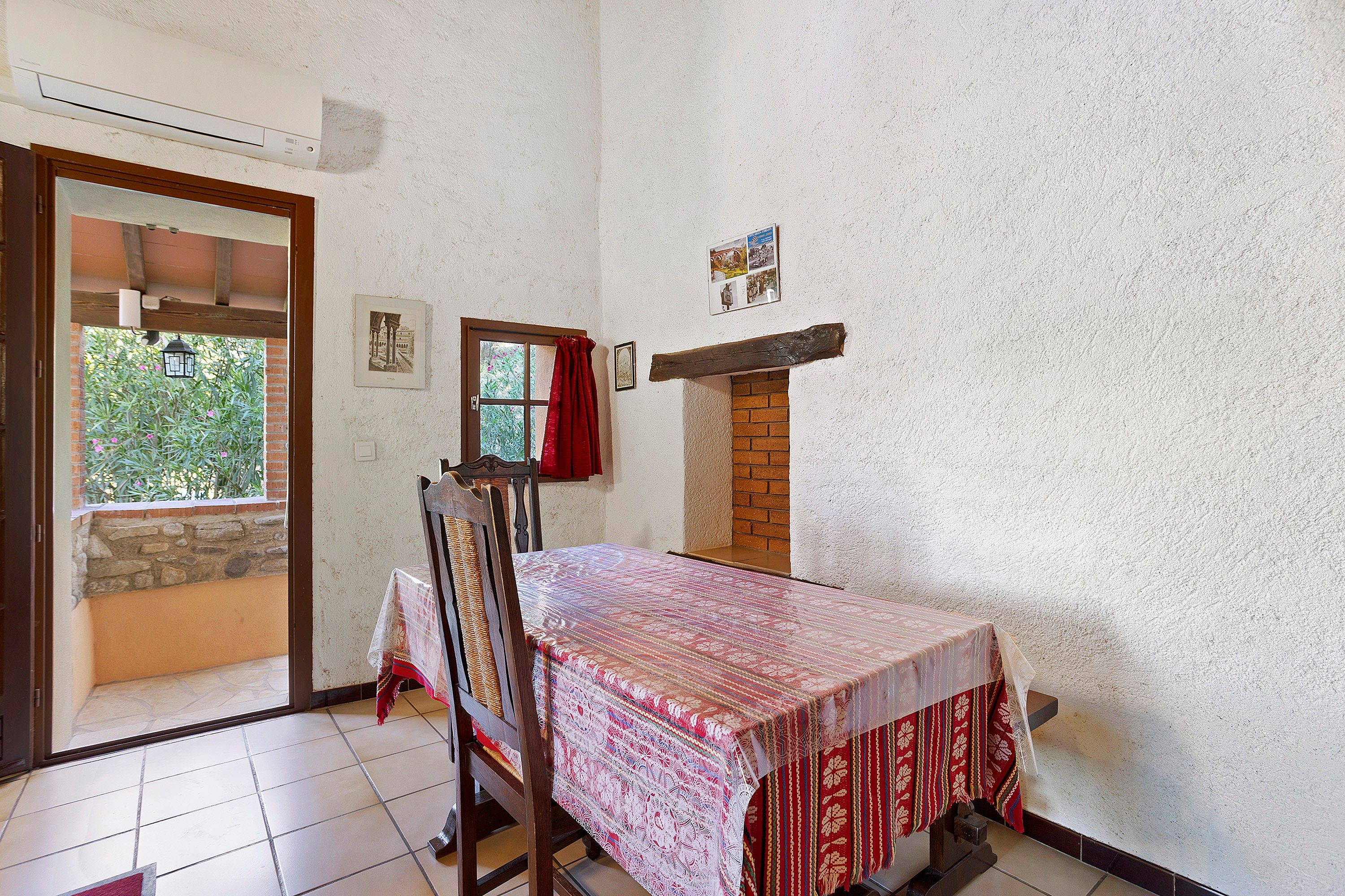 Ein Essbereich mit einem Tisch für zwei Personen, einem Holzstuhl, einem roten Vorhang und einem kleinen Fenster mit Blick auf Grünflächen.