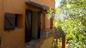 A building with a stone staircase leading to a door, a small window with shutters, and a tree in the foreground.