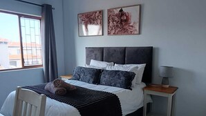 Un dormitorio con cama, mesita de noche, lámpara y dos cuadros enmarcados en la pared.
