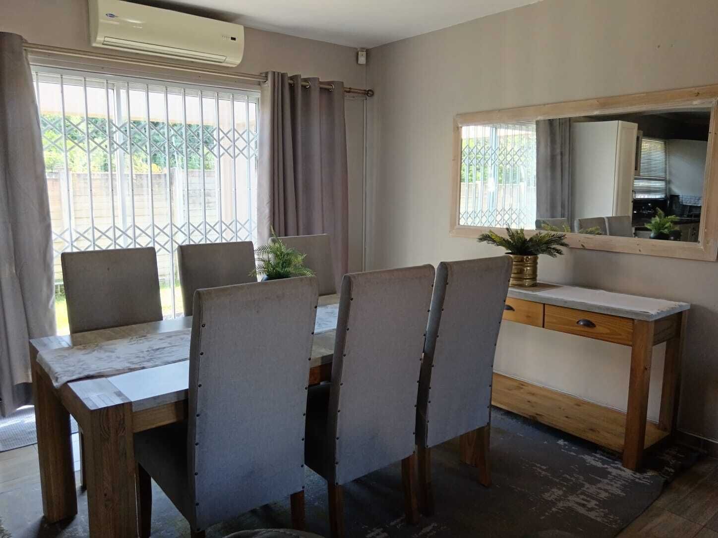Een eethoek met een houten tafel en stoelen, een kastje en een raam met gordijnen.