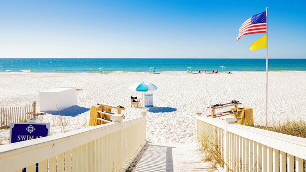 Ein Strand mit einer Holzpromenade, Liegestühlen, Sonnenschirmen und einer amerikanischen Flagge.