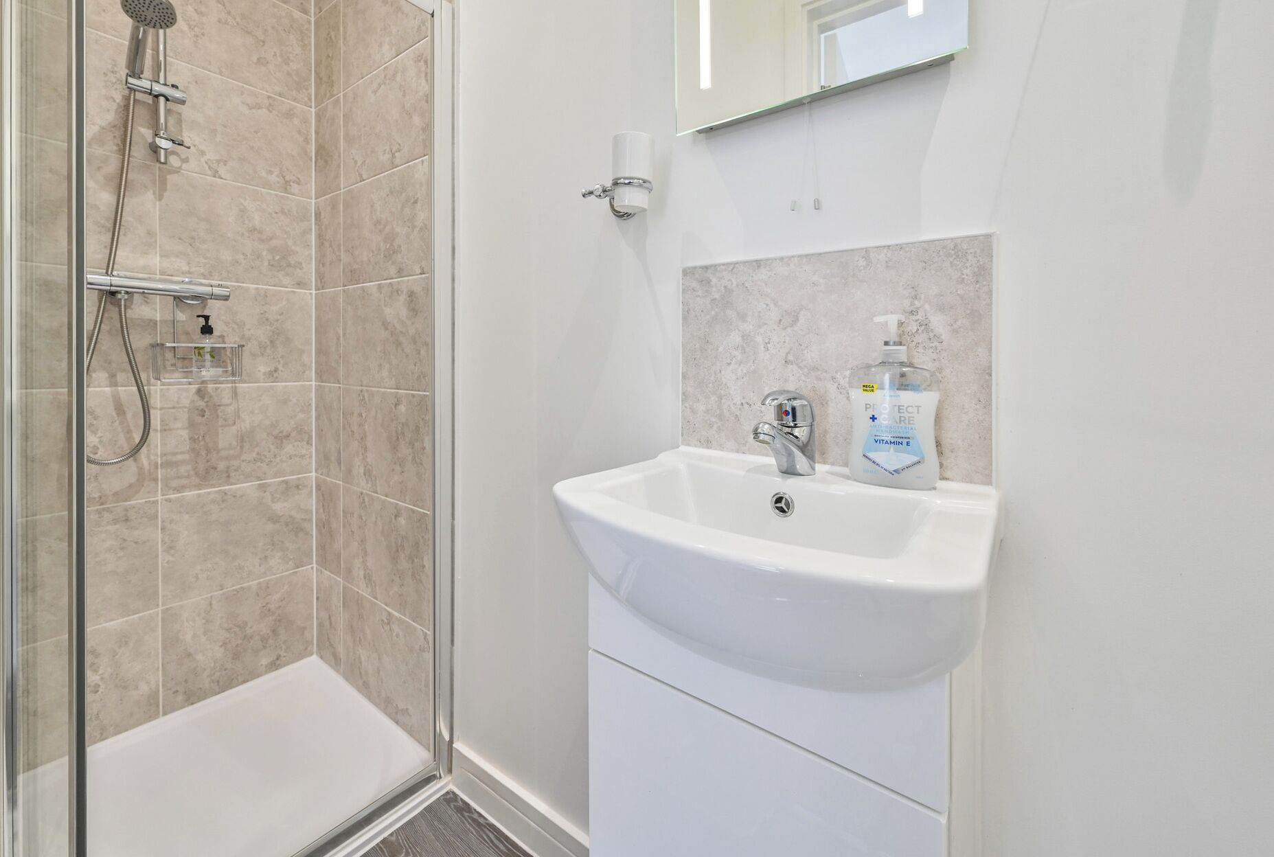 Een badkamer met een douche, wastafel en spiegel.