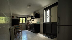 A kitchen with dark cabinets, a refrigerator, a window, and a chair. - The House Before the Sea (Fiumefreddo Sicilia)