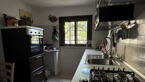 A kitchen with a stove, sink, and oven. There is a window with a view of greenery outside. - The House Before the Sea (Fiumefreddo Sicilia)