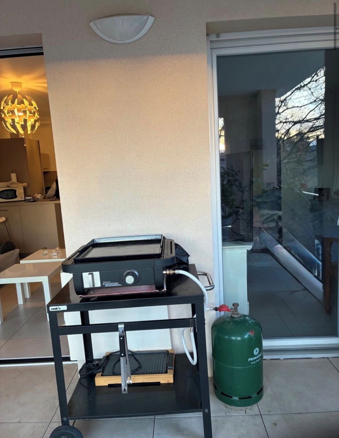 A modern kitchen with a built-in grill, a gas cylinder, and a dining area with a sofa and table.