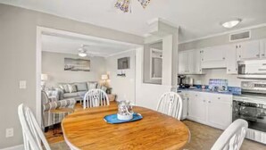 A modern kitchen with white cabinets and a dining area with a wooden table and white chairs. - Cozy 2-bedroom condo at Myrtle Beach Resort (Myrtle Beach)