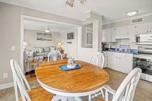 A modern kitchen with white cabinets and a dining area with a wooden table and white chairs. - Cozy 2-bedroom condo at Myrtle Beach Resort (Myrtle Beach)