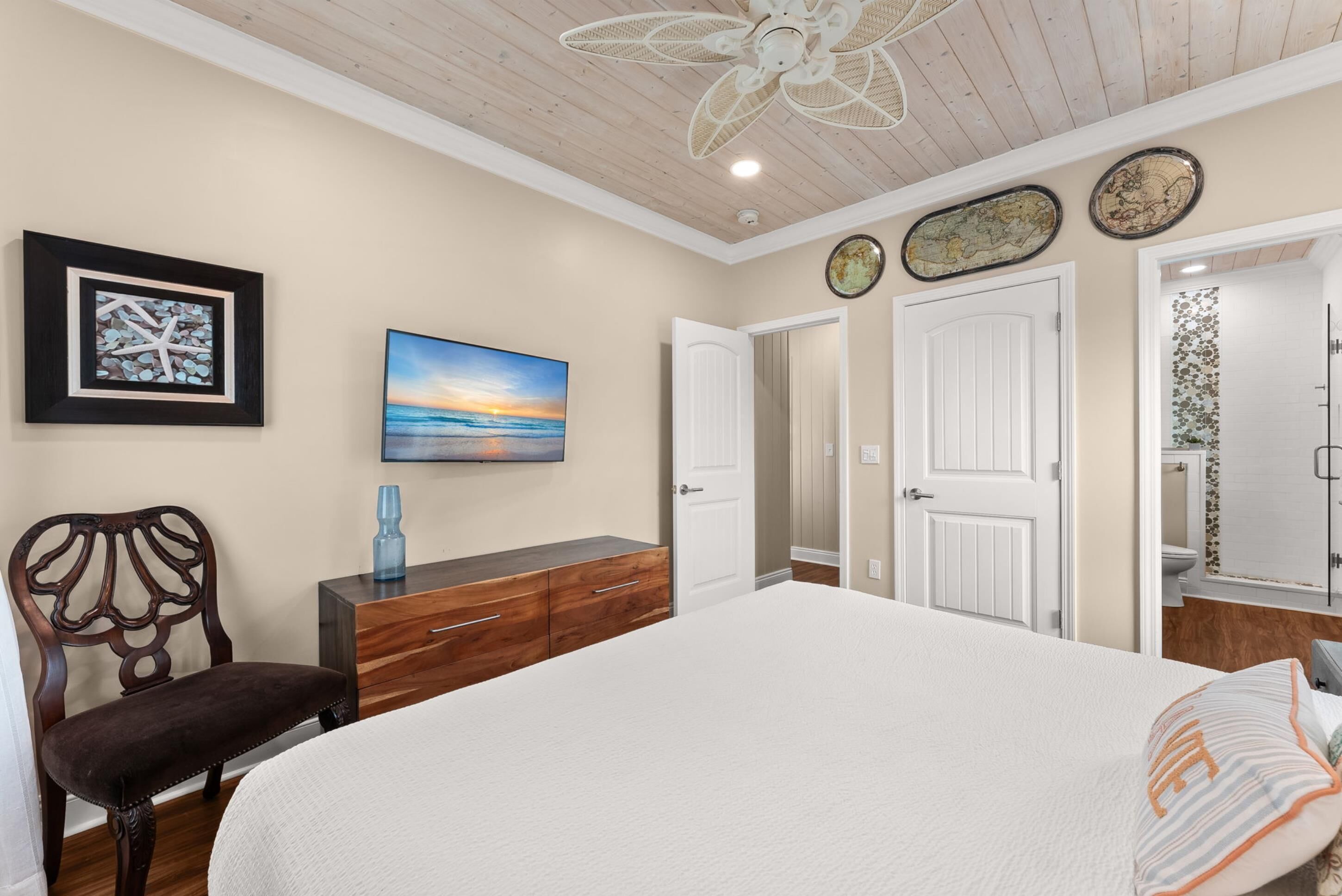 Quarto com cama, cômoda, cadeira, ventilador de teto e obras de arte nas paredes.
