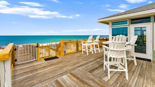 A wooden deck with white chairs and a glass door, overlooking a beach. - Beachfront House - Casa Bella Del Sol (Port St. Joe)