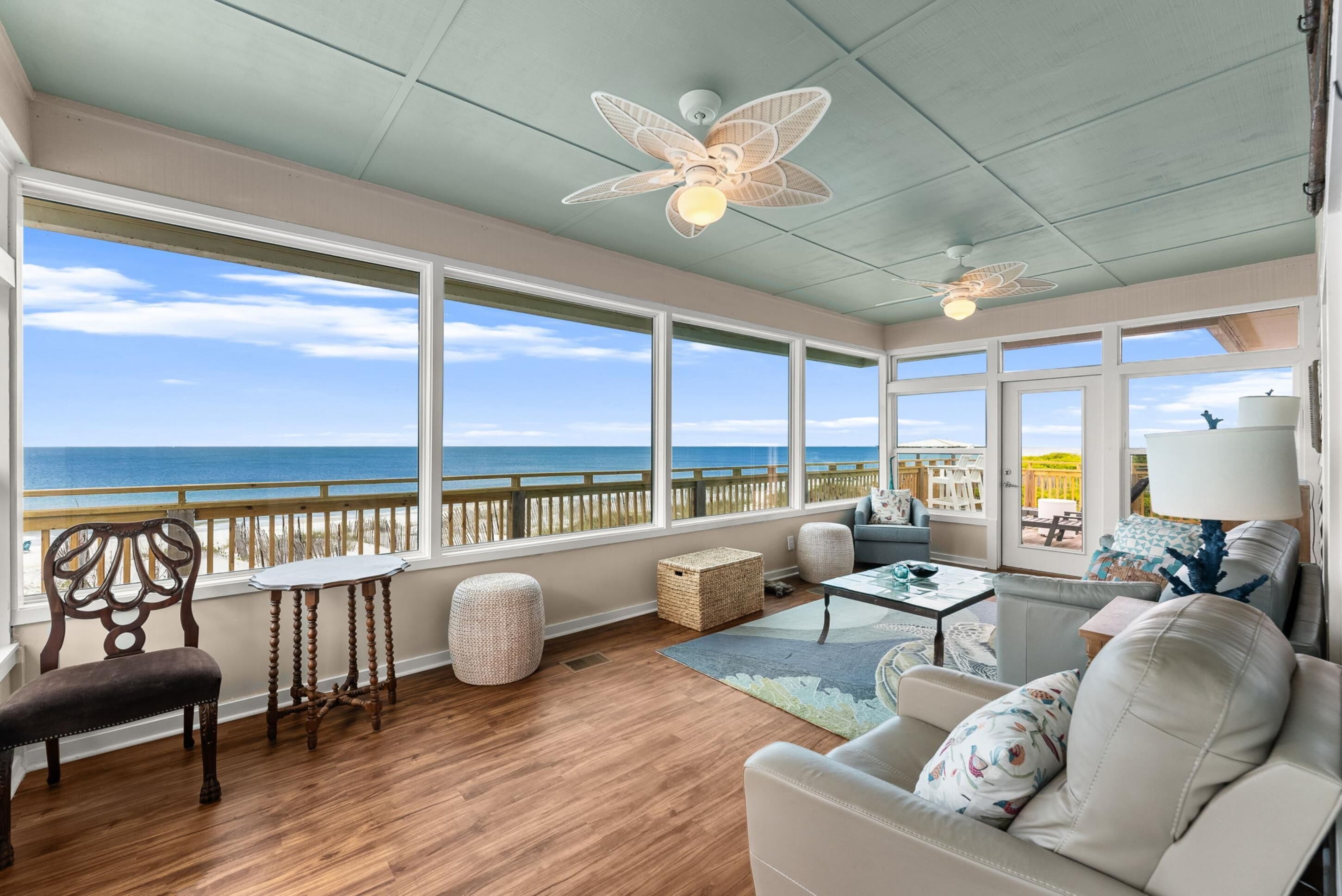 A spacious room with a large window overlooking the ocean, a ceiling fan, and a seating area with a table and chairs.