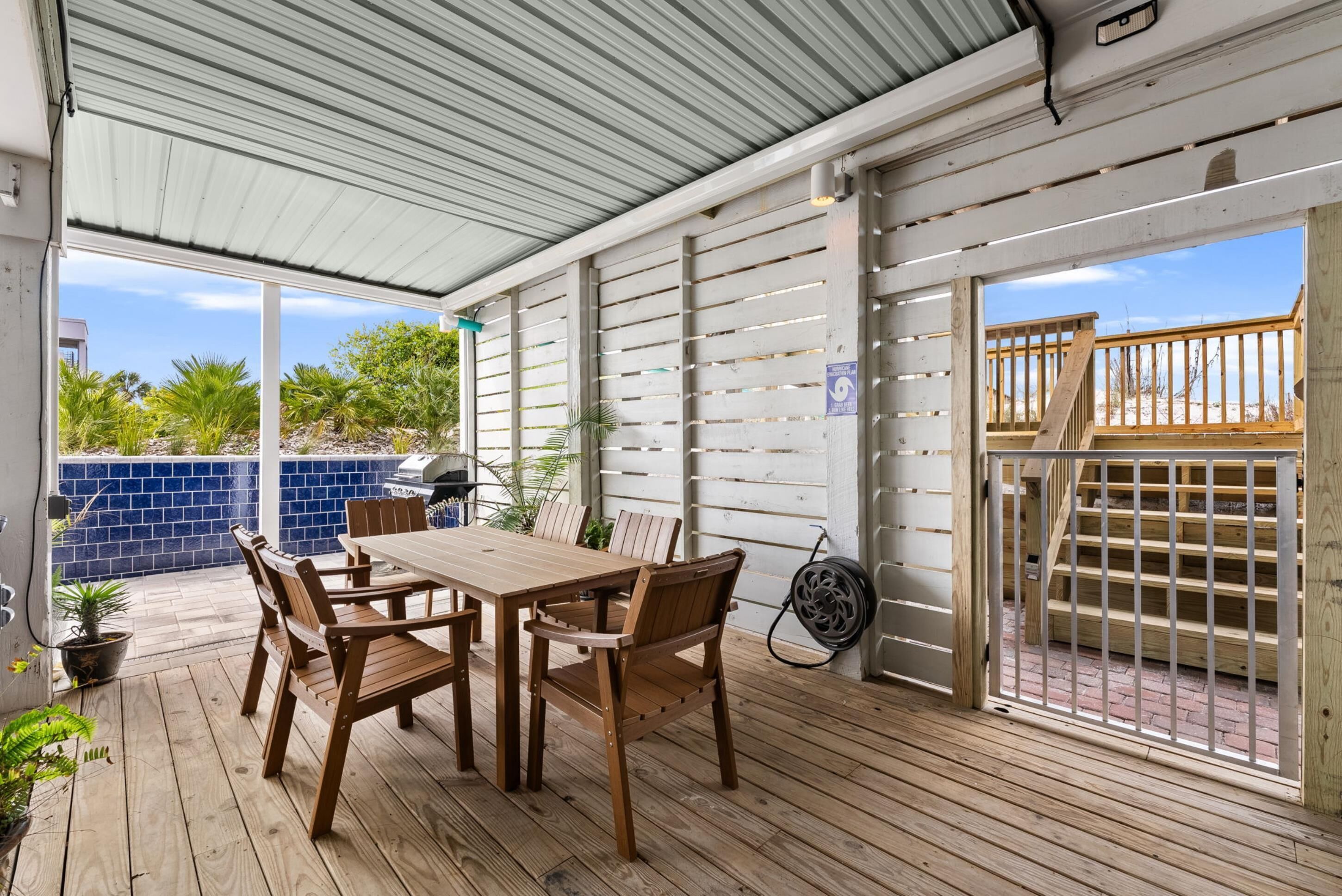 A covered patio with a wooden table and chairs, a grill, and a view of the beach.