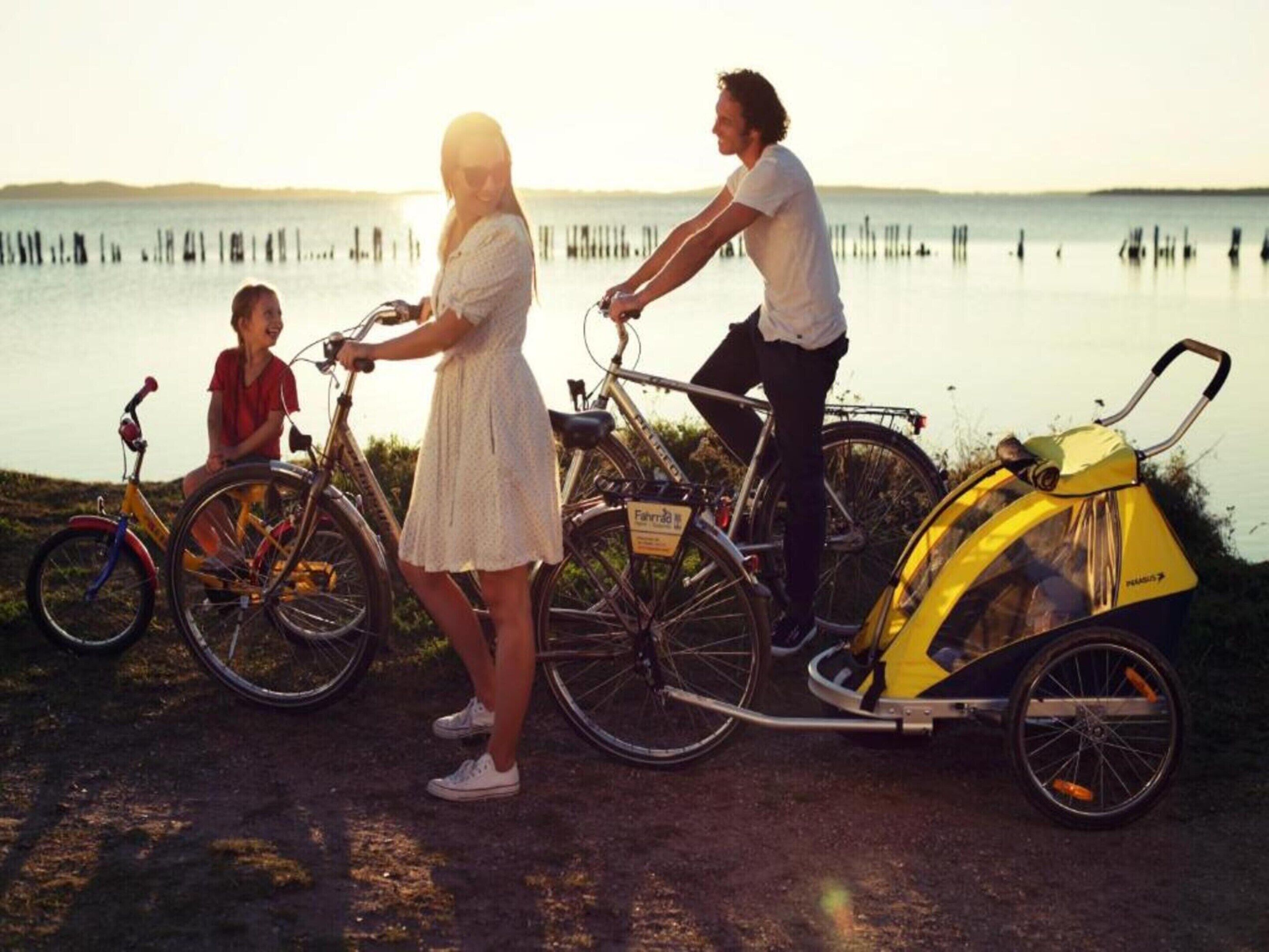 Une famille avec des vélos et un tricycle, au bord d’un lac.