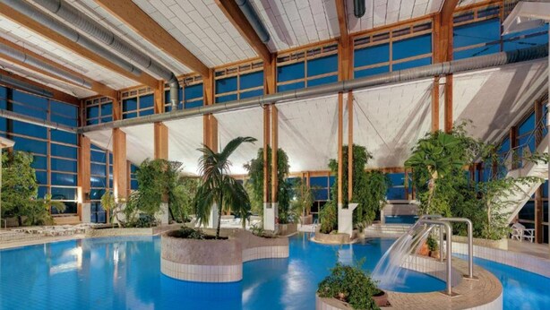 An indoor swimming pool with a central slide, surrounded by plants and a high ceiling with wooden beams. - Sunday Resort Rugen 1-bedroom Apartment (Sagard)