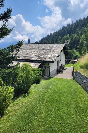 A rustic chalet with a stone roof, surrounded by lush greenery and a forested backdrop. - Alpe Monte Massella by Interhome (Poschiavo)