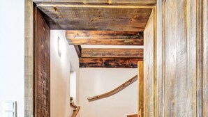 Un escalier en bois au design rustique, menant à une pièce dont un des murs est blanc et où se trouve un petit tapis au pied de l’escalier.