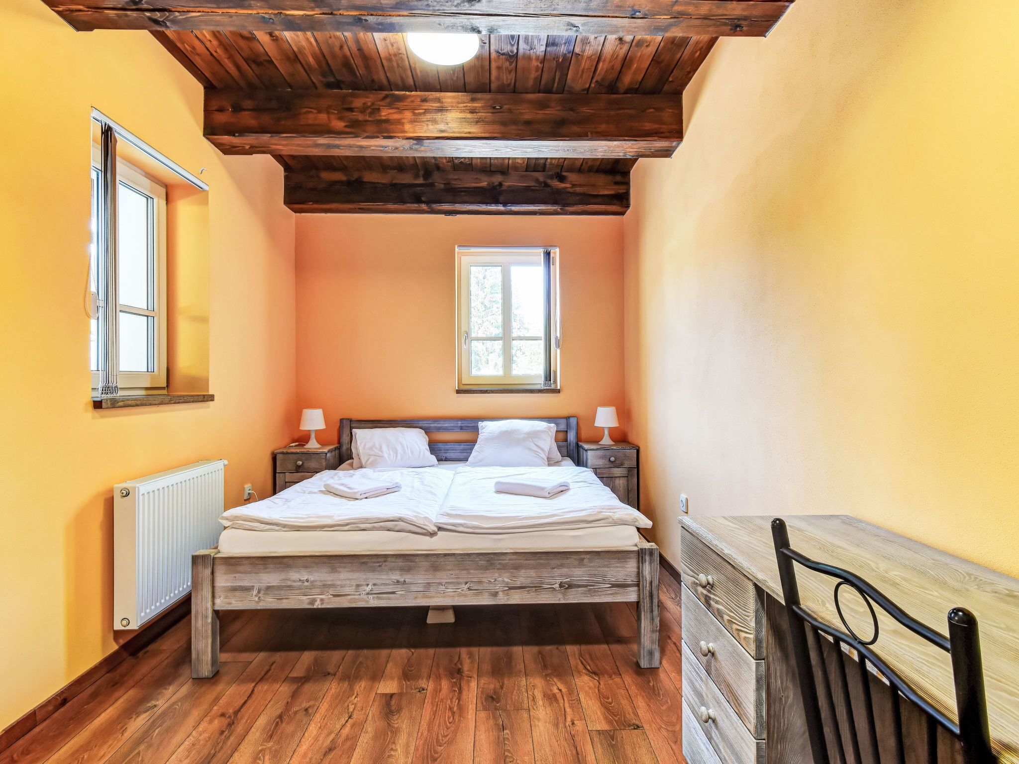 A bedroom with a wooden bed, two bedside tables with lamps, a radiator, and a window.