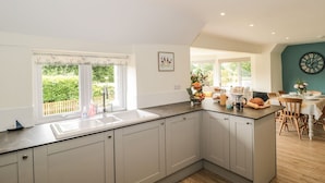A modern kitchen with a large island, a built-in sink, and a dining area with wooden chairs and a table. - Ammerham Farm Cottage (Chard)