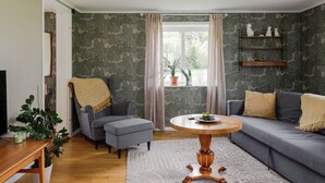 A living room with a grey sofa, a round wooden coffee table, a grey armchair, a wooden side table, and a potted plant.