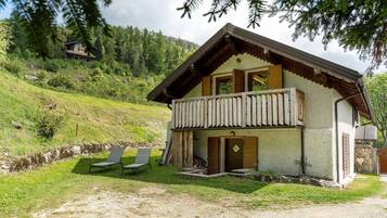 Un chalet a due piani con un balcone, un pontile in legno e un muro in pietra.