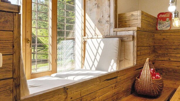 Interior de una cabaña de madera con un asiento junto a la ventana, una cesta tejida y un cartel de Coca-Cola.
