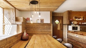 Un interior de madera con una mesa larga, sillas, un microondas y una ventana con luz natural.