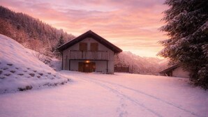 Una cabaña de madera con balcón, rodeada de árboles cubiertos de nieve y un cielo despejado.