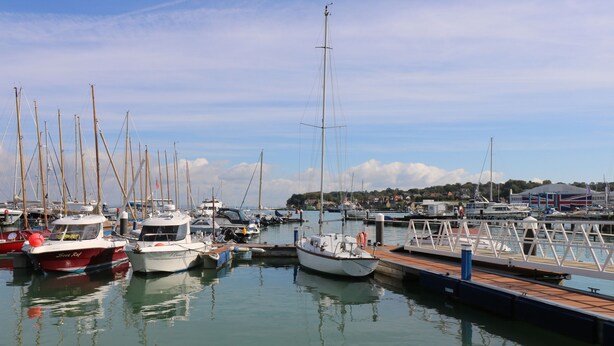 A marina with multiple boats docked, a wooden pier, and a distant town. - Red Brick Haven (East Cowes)