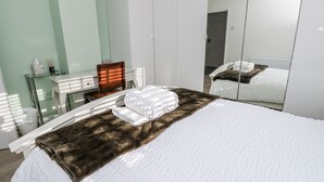 A hotel room with a bed, a desk, a chair, a mirror, and a wardrobe. - Red Brick Haven (East Cowes)