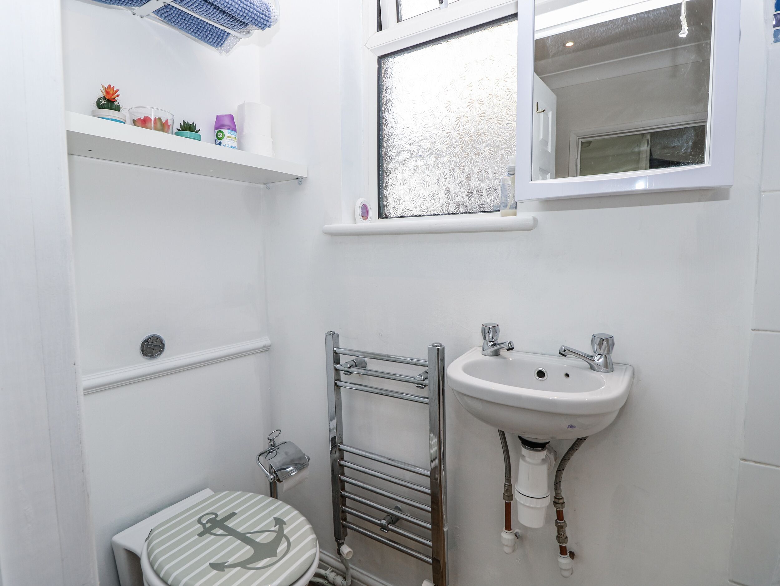 A bathroom with a toilet, a sink, a towel rack, and a shelf with toiletries.