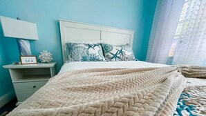 Un letto con una coperta beige, un comodino bianco con una lampada e un cartello con la scritta 'SEA'.