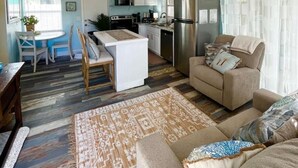 Un soggiorno moderno con divano, zona pranzo con tavolo e sedie, cucina completa di elettrodomestici e ventilatore a soffitto.