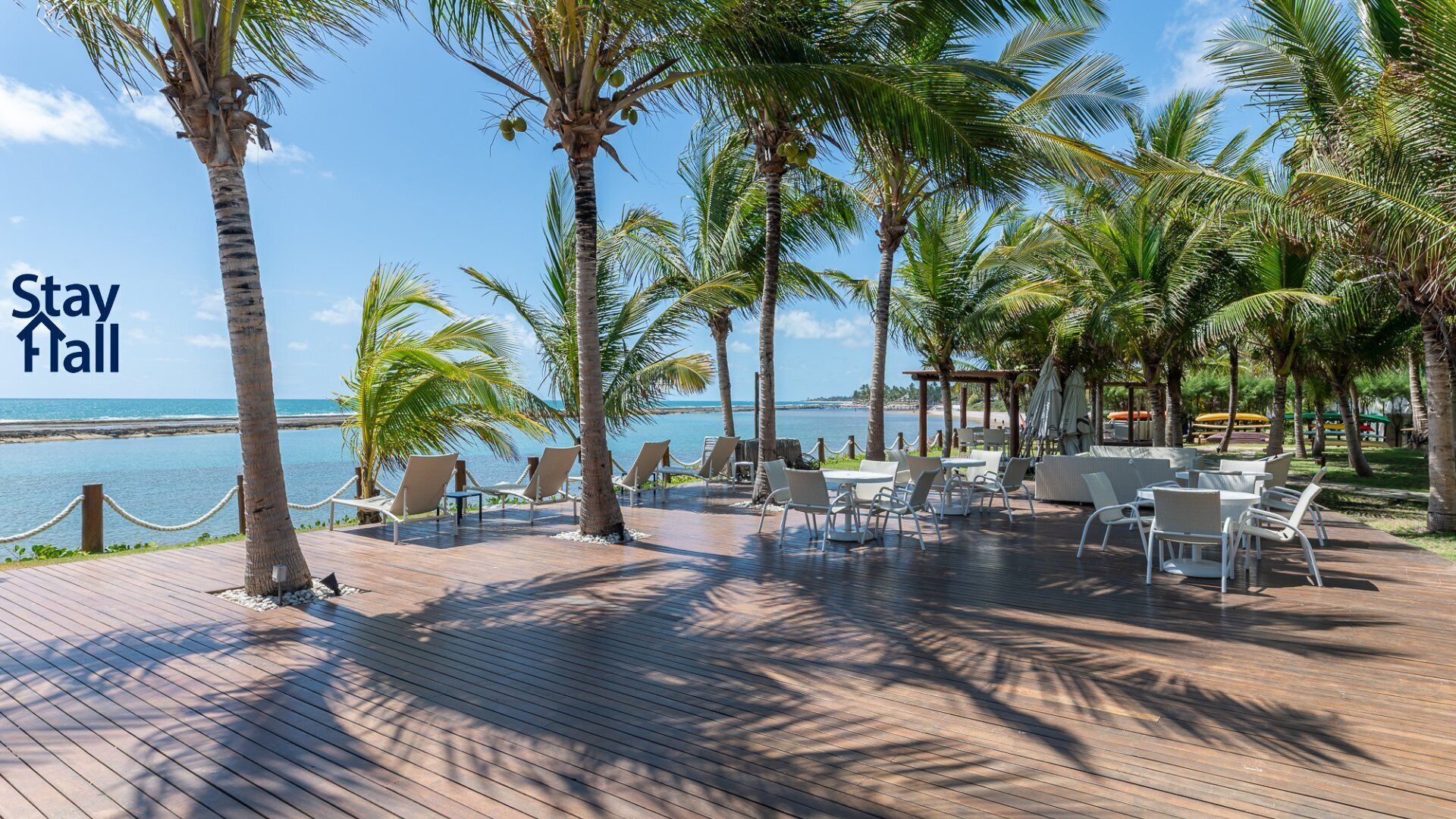 A wooden deck with outdoor seating, palm trees, and a view of the ocean.