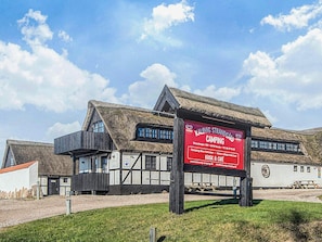 Een traditioneel gebouw met rieten dak, een bord met daarop een advertentie voor een camping en een kleine kiosk.