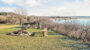 A lakeside park with a picnic area, a thatched structure, and a view of a distant bridge. - Standard Cabin For, 5 Pers, 25m2 (Ronde)