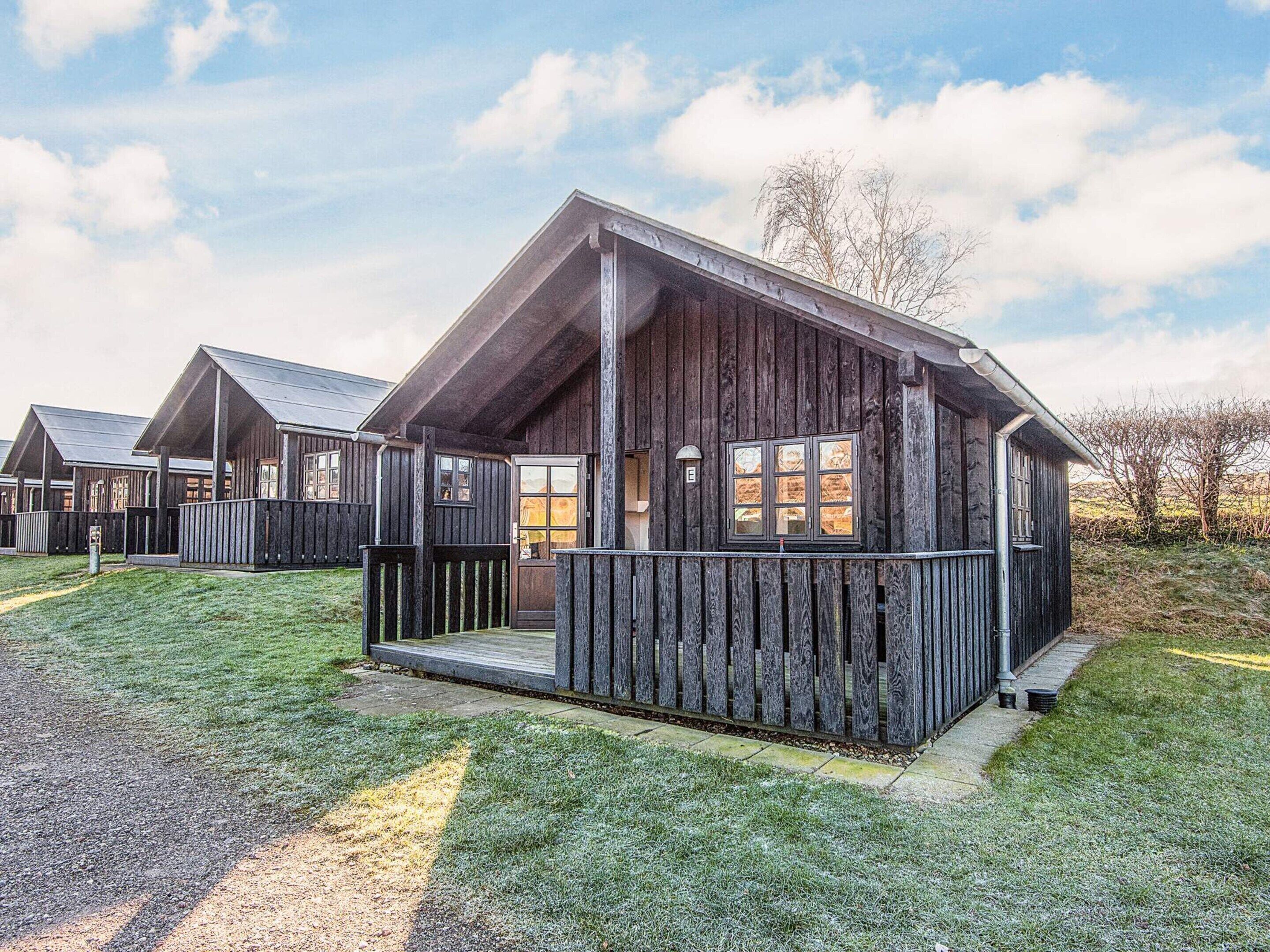 Een rij houten blokhutten met een veranda, gelegen in een grasrijk gebied onder een heldere lucht.