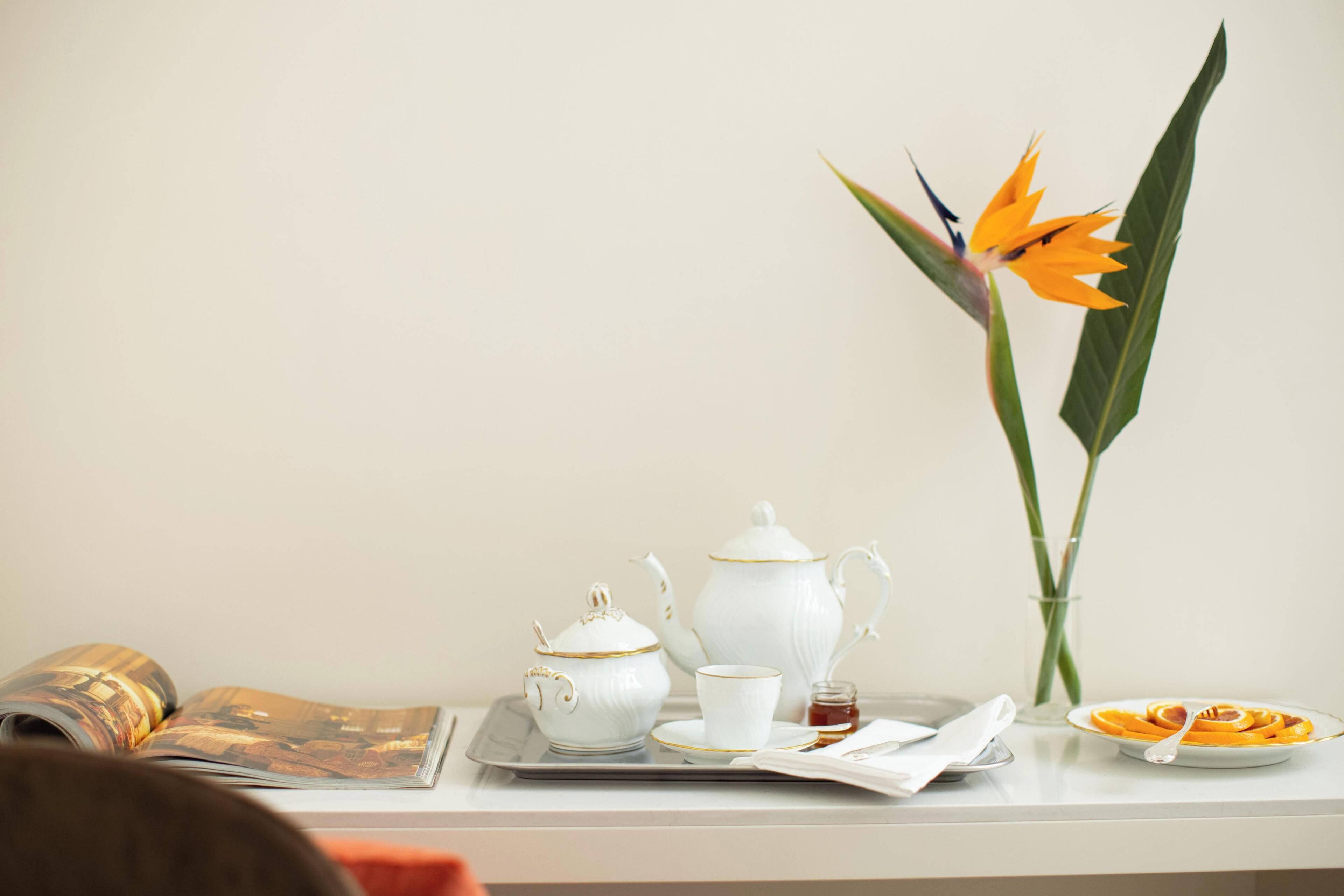 A tray with a teapot, cup, and saucer, a plate with food, and a flower vase on a table.