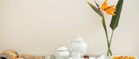 A tray with a teapot, cup, and saucer, a plate with food, and a flower vase on a table.