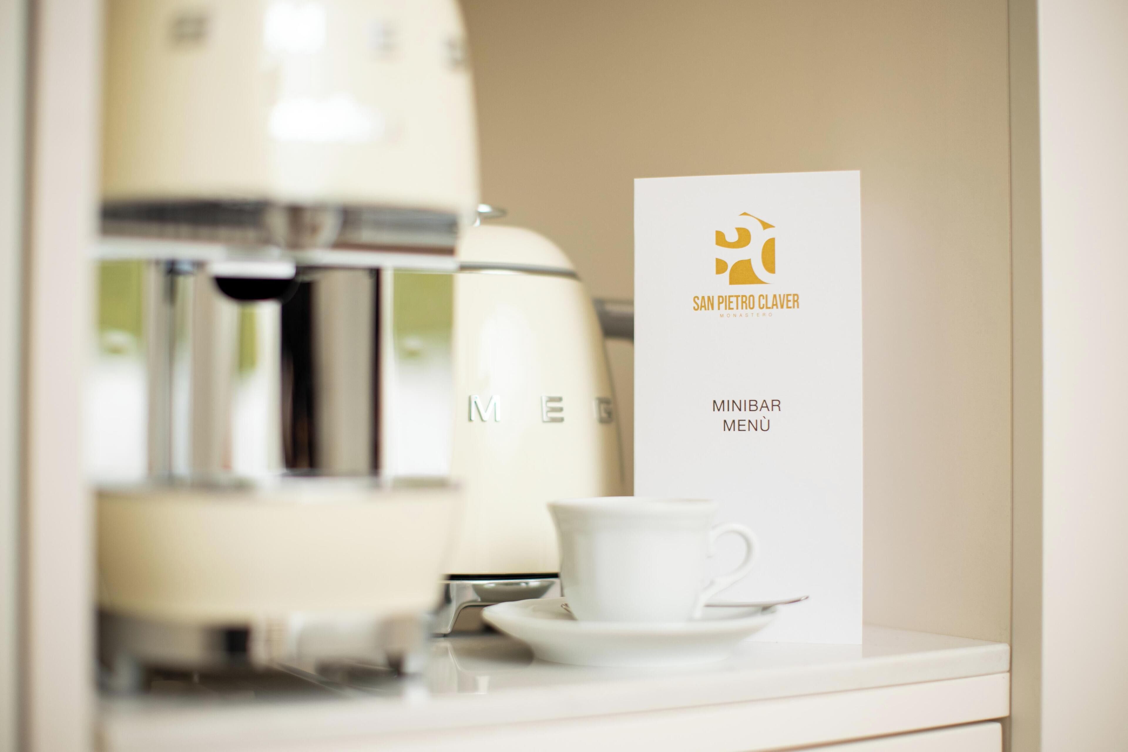 Une machine à café, une tasse et un panneau affichant le menu avec les inscriptions « SAN PIERRO CLAVER » et « MINIBAR MENÜ ».