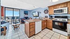 A modern kitchen with a dishwasher, stove, and microwave. There's a dining area with a table and chairs, and a large window overlooking a scenic view. - 1BR/1B~sleeps 4~Boat Parking~Pool~Pickleball! (Gulf Shores)