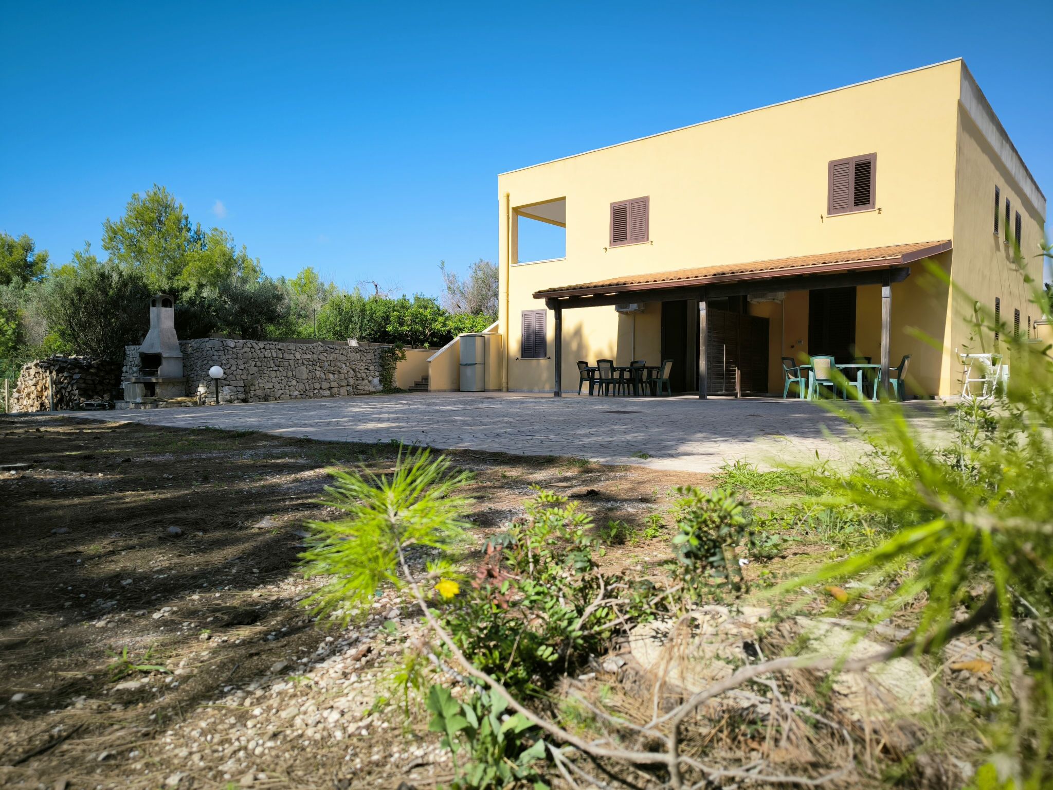 A modern two-story house with a patio area, outdoor seating, and a stone wall.