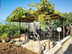 Ein überdachter Sitzbereich im Freien mit einer Pergola, einem Grill und einem Blumentopf.
