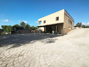 Un edificio a due piani con tetto piatto, un’area patio con mobili da esterno e un muro in pietra sullo sfondo.