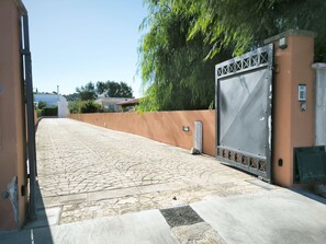 Ein gepflasterter Weg führt zu einem verschlossenen Eingang mit einem Metalltor und einer Mauer mit einem kleinen Fenster.