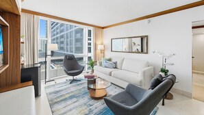 Ein modernes Hotelzimmer mit großem Fenster, einem weißen Sofa, einem grauen Sessel, einem Glastisch und einem Spiegel an der Wand.
