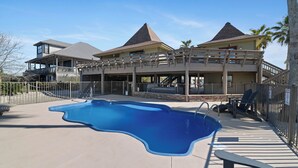 Uma piscina grande com formato singular, rodeada por um espaço coberto com área de estar.