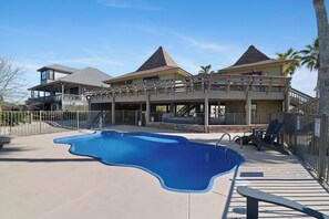 A large swimming pool with a unique shape, surrounded by a covered patio area with seating. - TikiTime by Liquid Life (Gulf Shores)