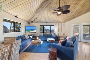 Un soggiorno spazioso con soffitto in legno, un grande televisore, un divano e vista sull'oceano.